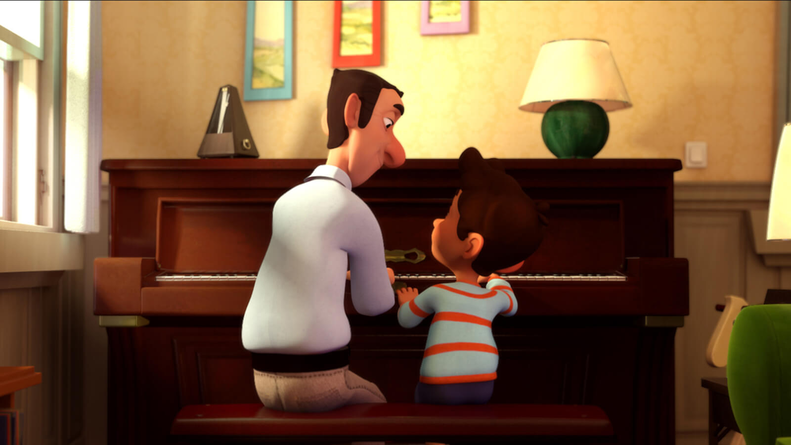 The backs of a man in a white shirt and a boy in a blue and red striped t-shirt as they sit at a brown wooden upright piano