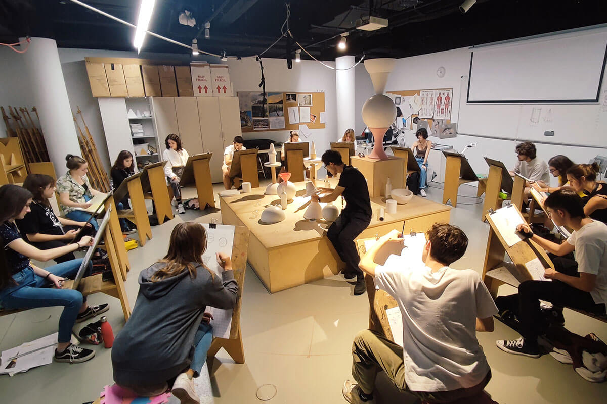 A group of BFA students sit in front of easels sketching objects.