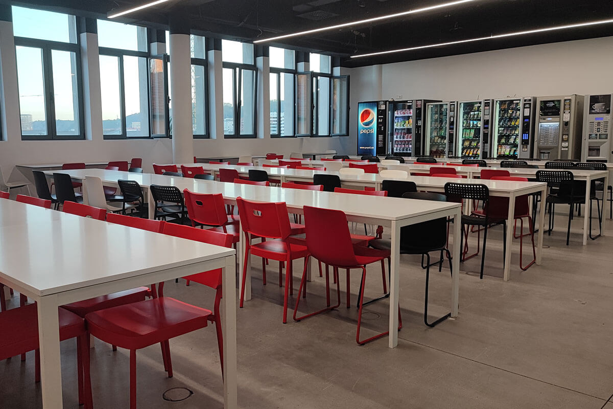 An empty canteen with various long tables and vending machines.
