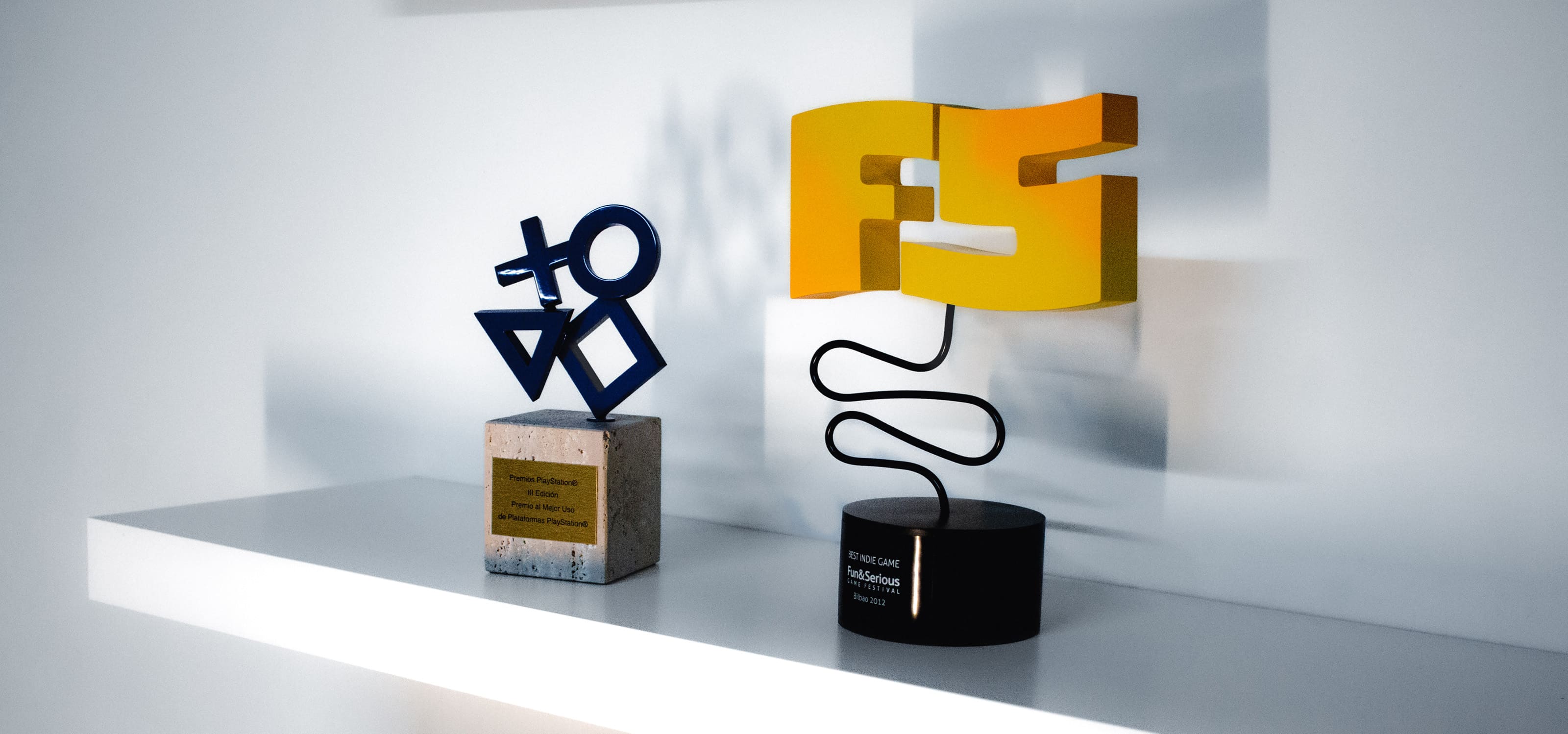 Display of awards obtained by students of Digipen Europe-Bilbao in games and animations placed on a white shelf and white background with a shadow play.