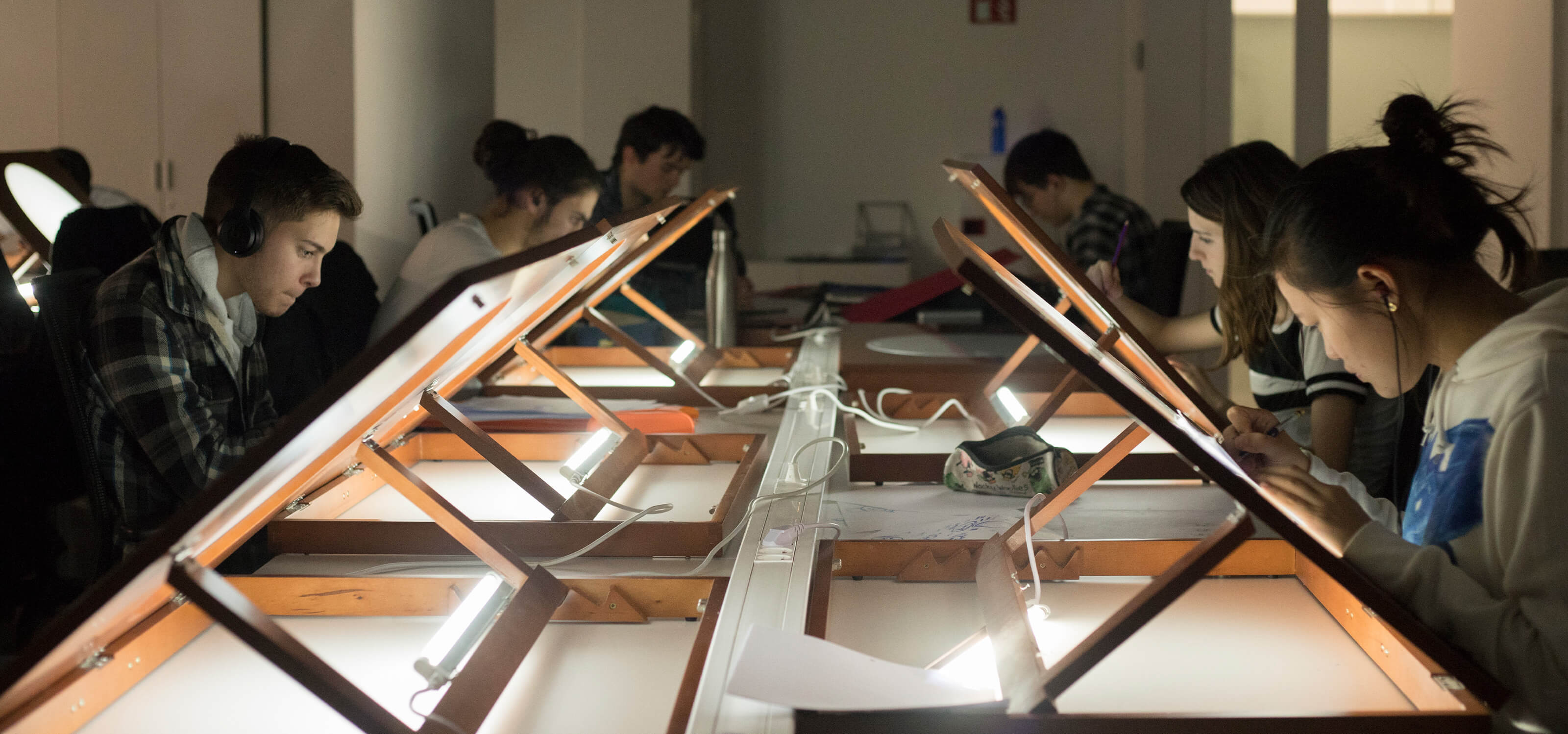 Several students use drawing tables with backlights to work on their designs.