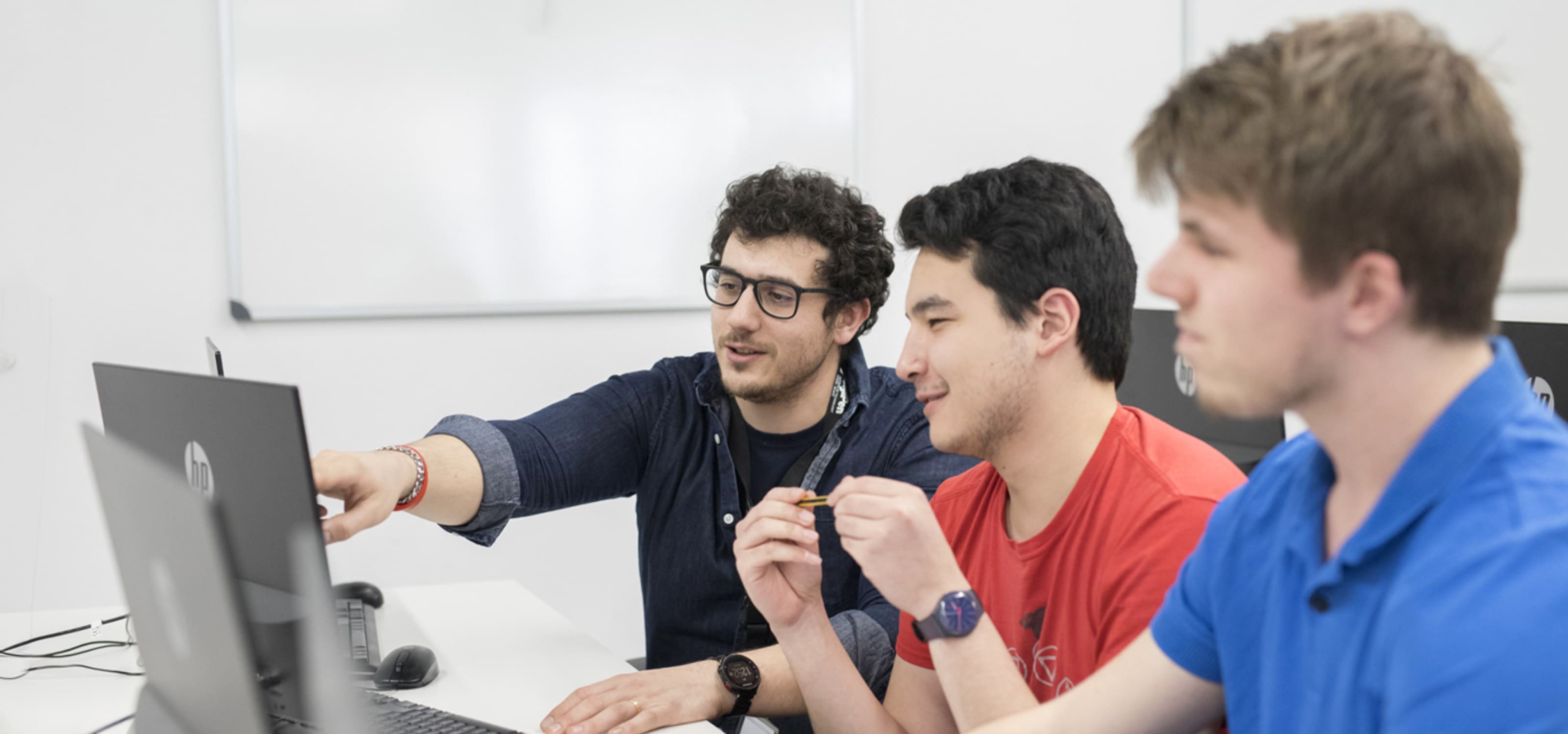 Un profesor de DigiPen Europe-Bilbao comparte conocimiento con dos estudiantes mientras trabajan con sus portátiles.