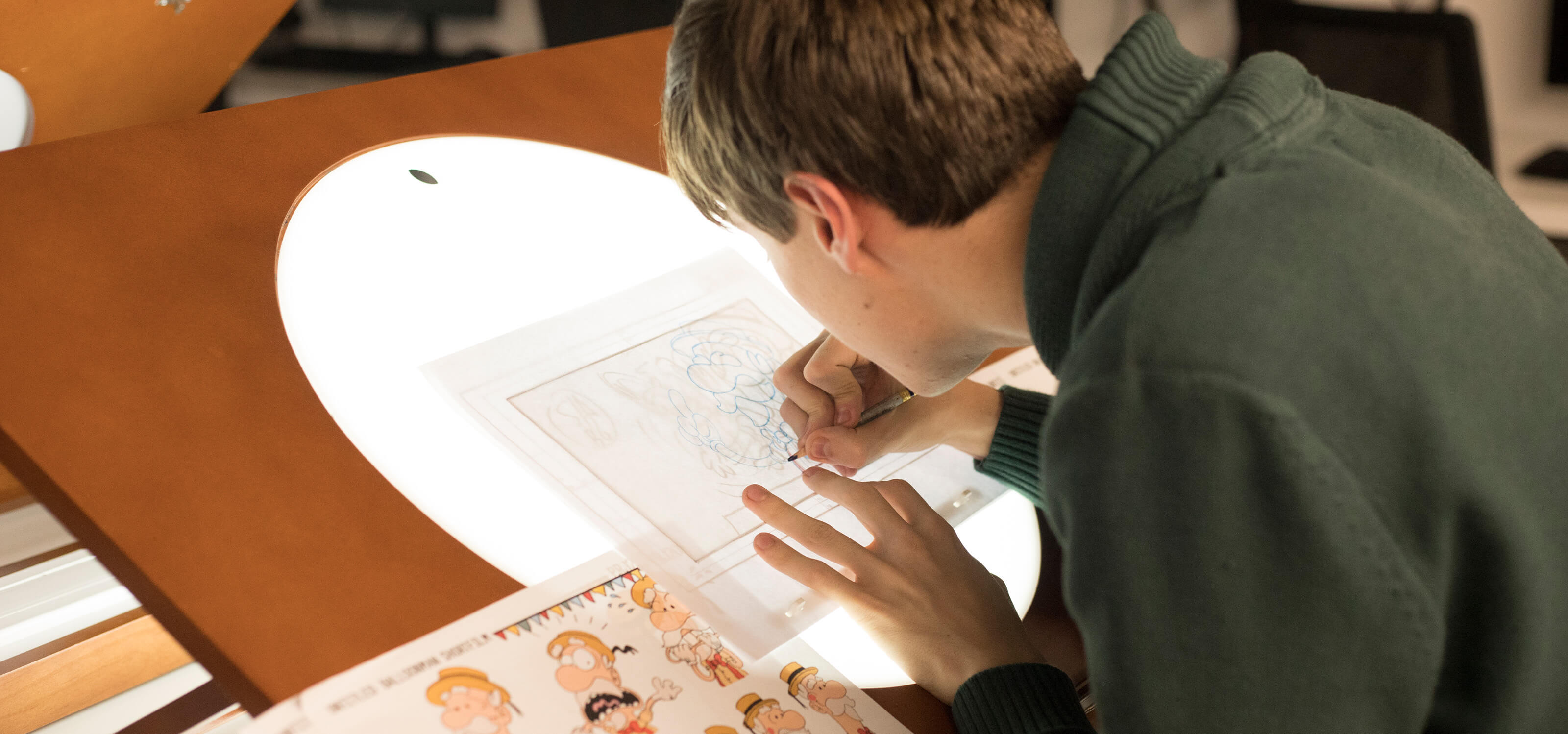 Un estudiante usa una mesa de dibujo con luz de fondo para delinear el diseño de un personaje.