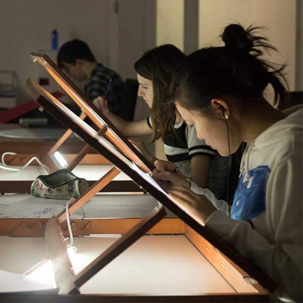 Several students use drawing tables with backlights to work on their designs