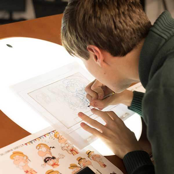 Un estudiante usa una mesa de dibujo con luz de fondo para delinear el diseño de un personaje
