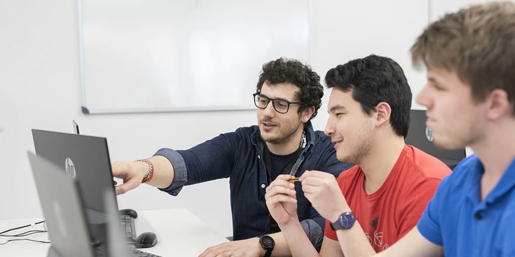 Un profesor de DigiPen Europe-Bilbao comparte conocimiento con dos estudiantes mientras trabajan con sus portátiles