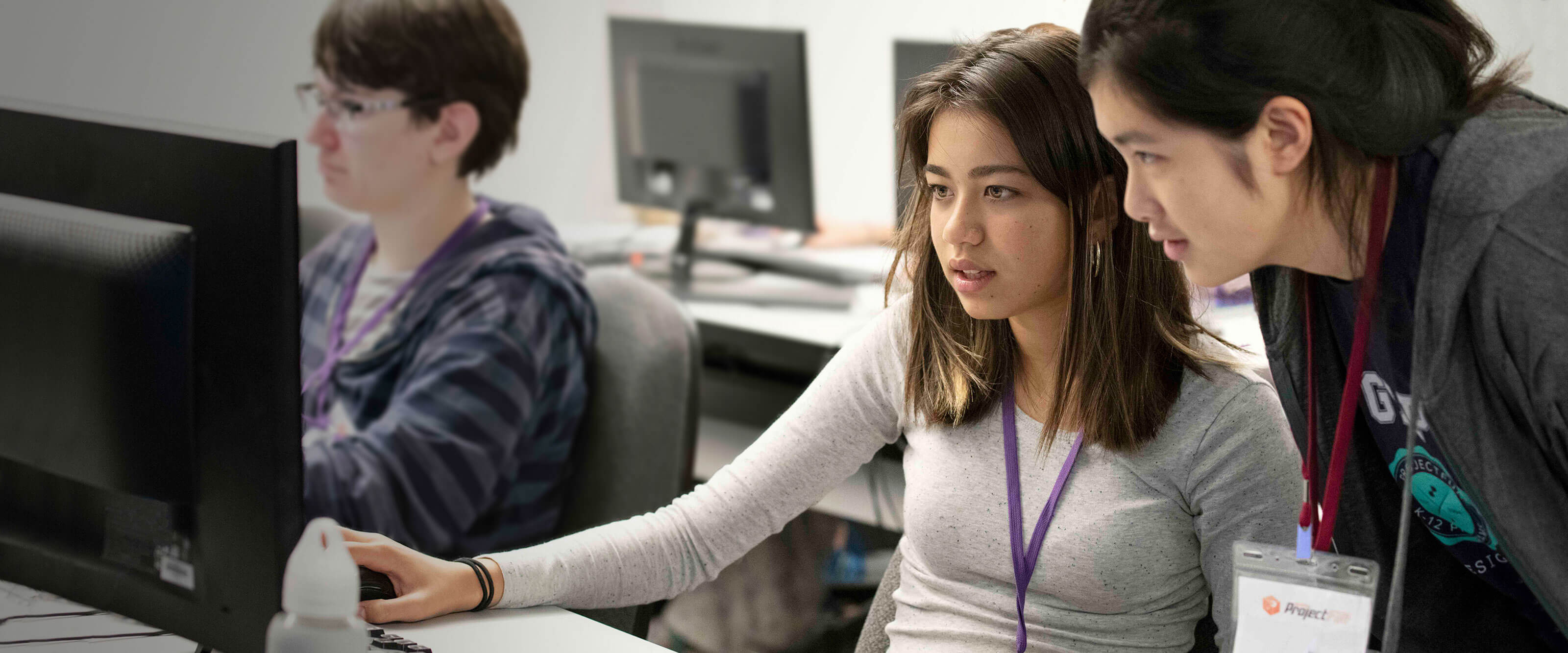A student sits in front of a computer monitor as a ProjectFUN instructor stands over her shoulder.