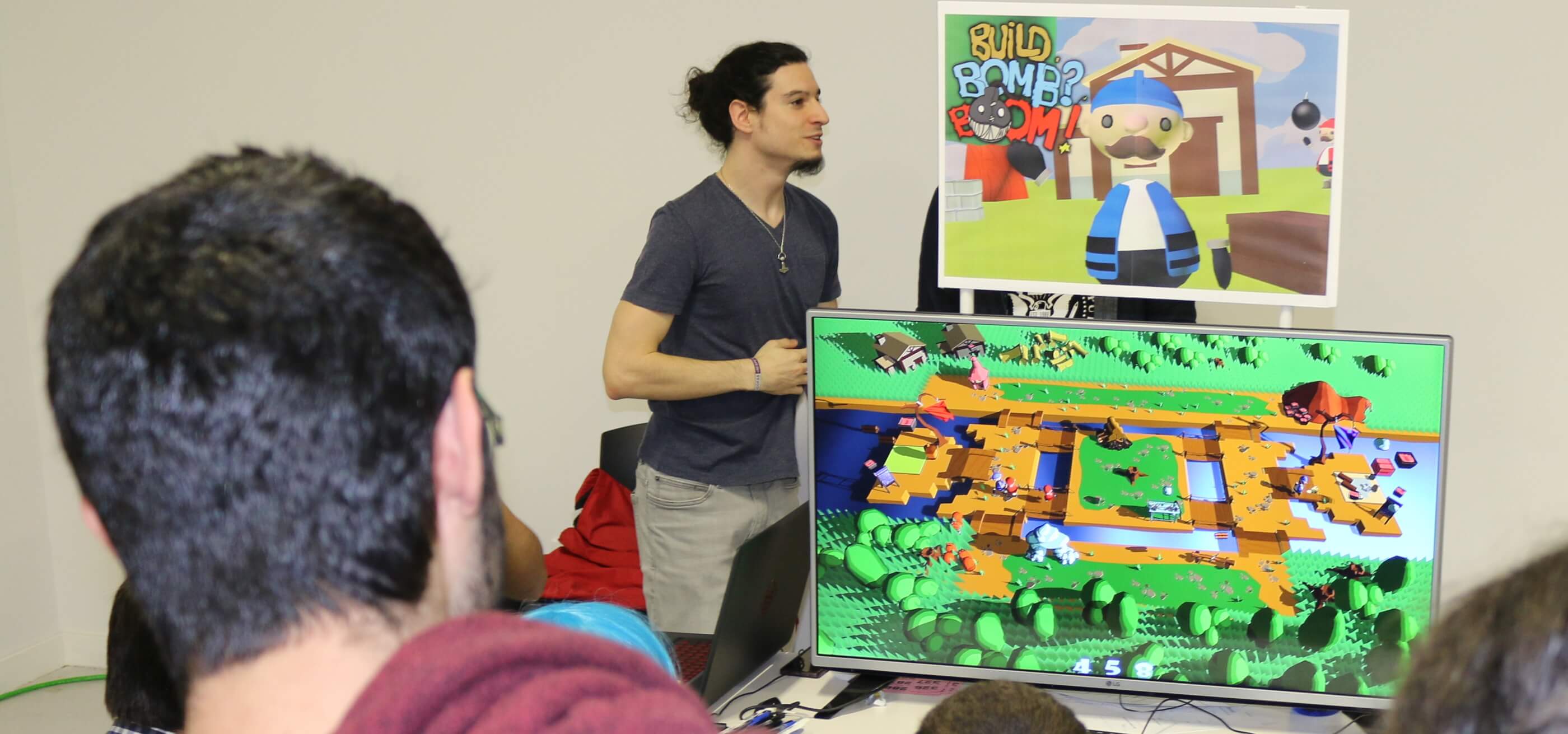 A DigiPen Bilbao student stands next to a television with a student game playing onscreen
