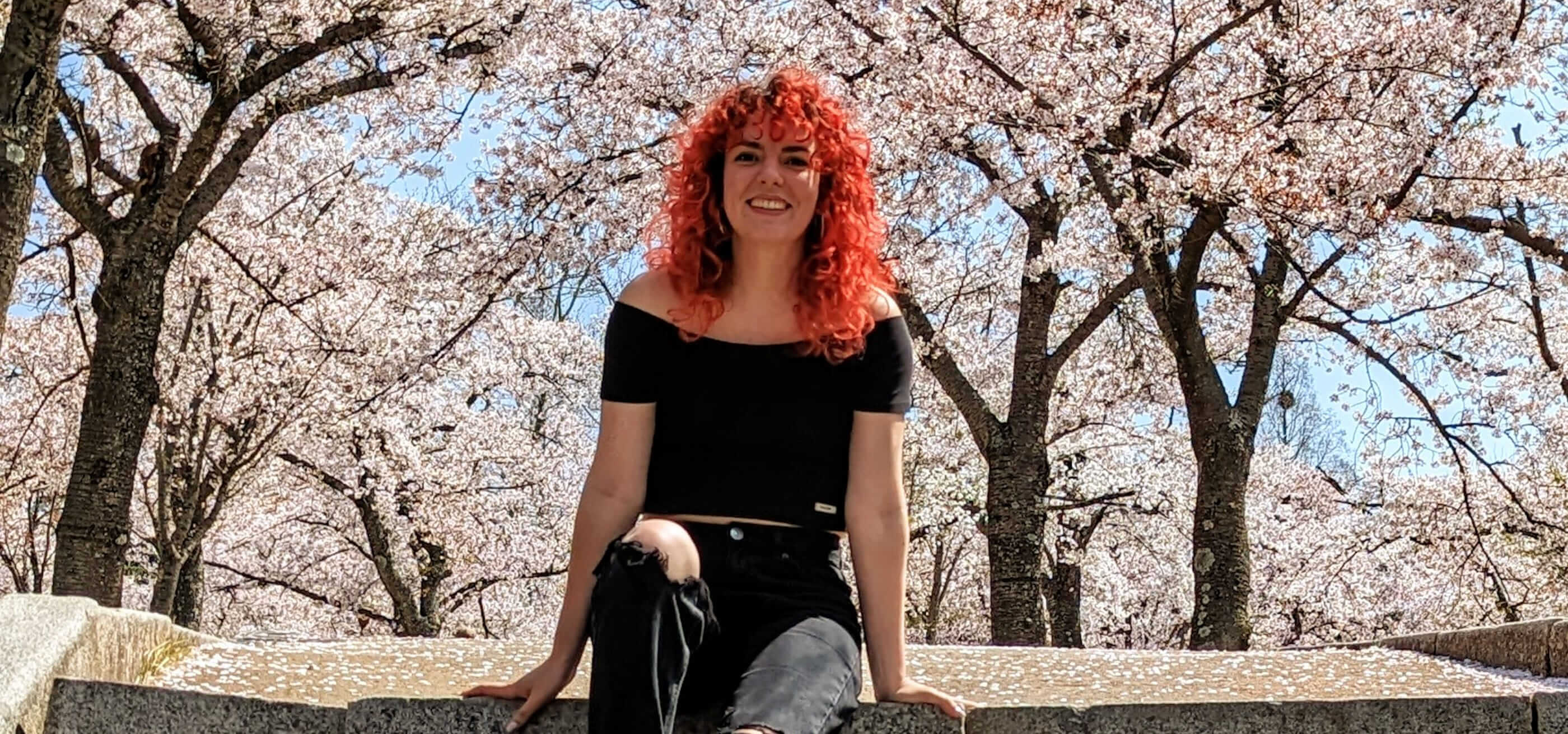 DigiPen graduate Marina Bordona standing in a beautiful cherry blossom garden.