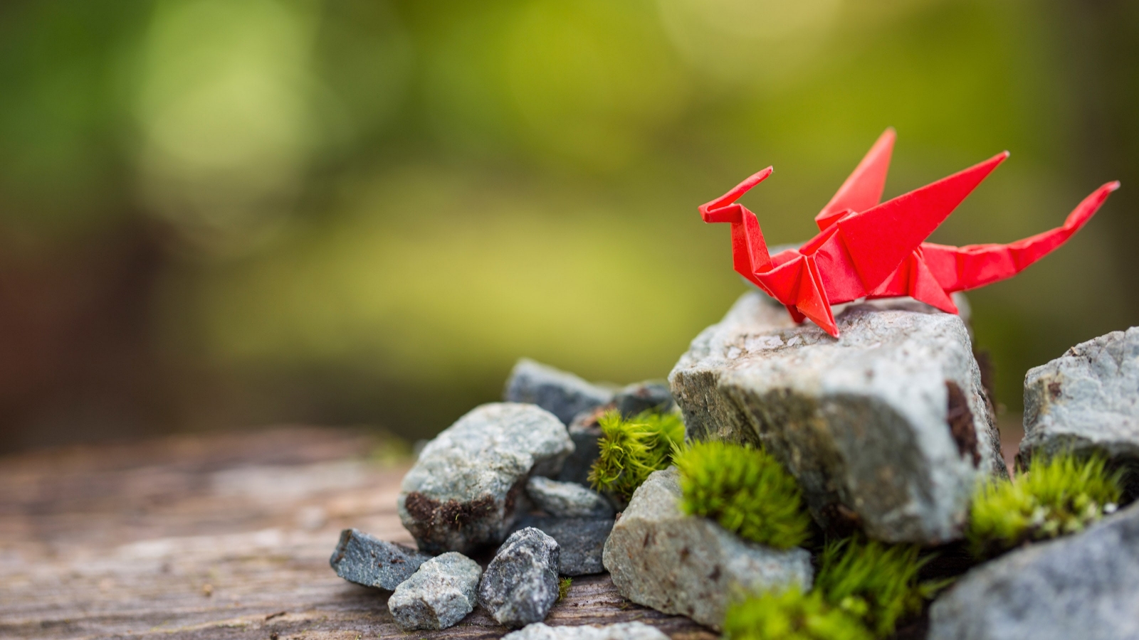 A dragon crafted from red origami paper sitting on a mossy rock.