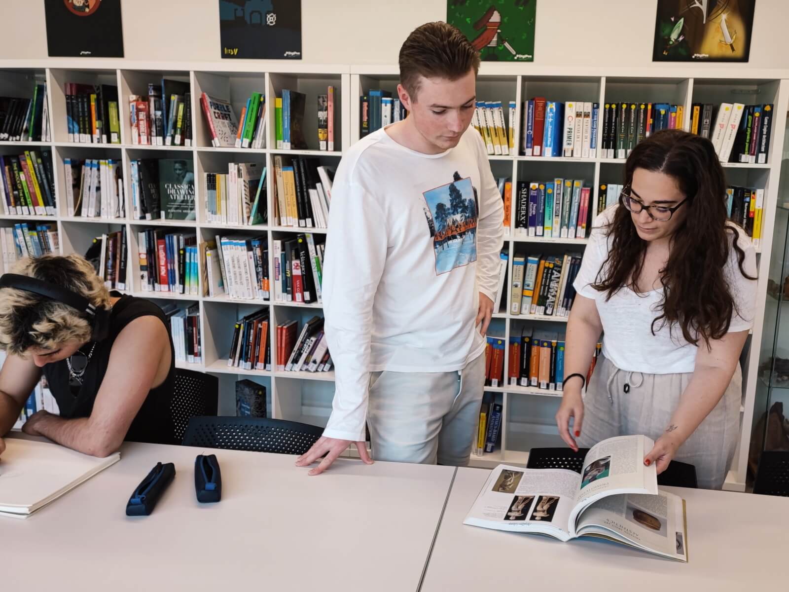 Un estudiante y la bibliotecaria ojean un libro en de la biblioteca de DigiPen Europe-Bilbao