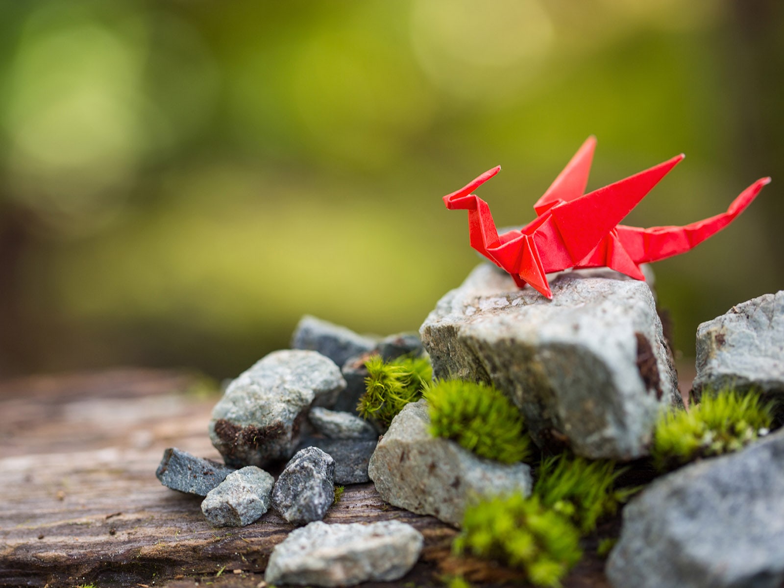 Un dragón de papel origami rojo sobre una roca cubierta de musgo.