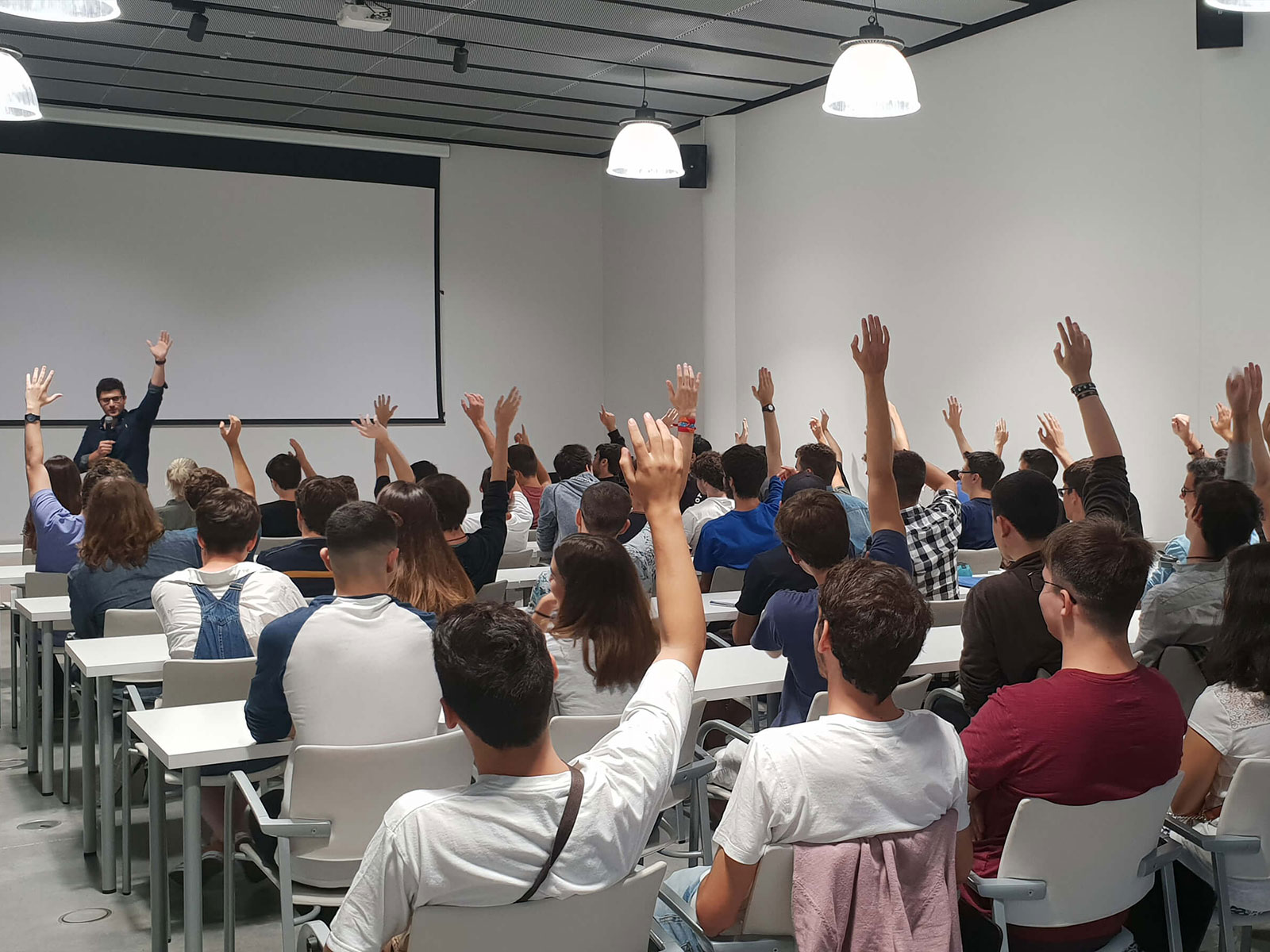 Un profesor frente a un grupo de estudiantes que están sentados con las manos levantadas