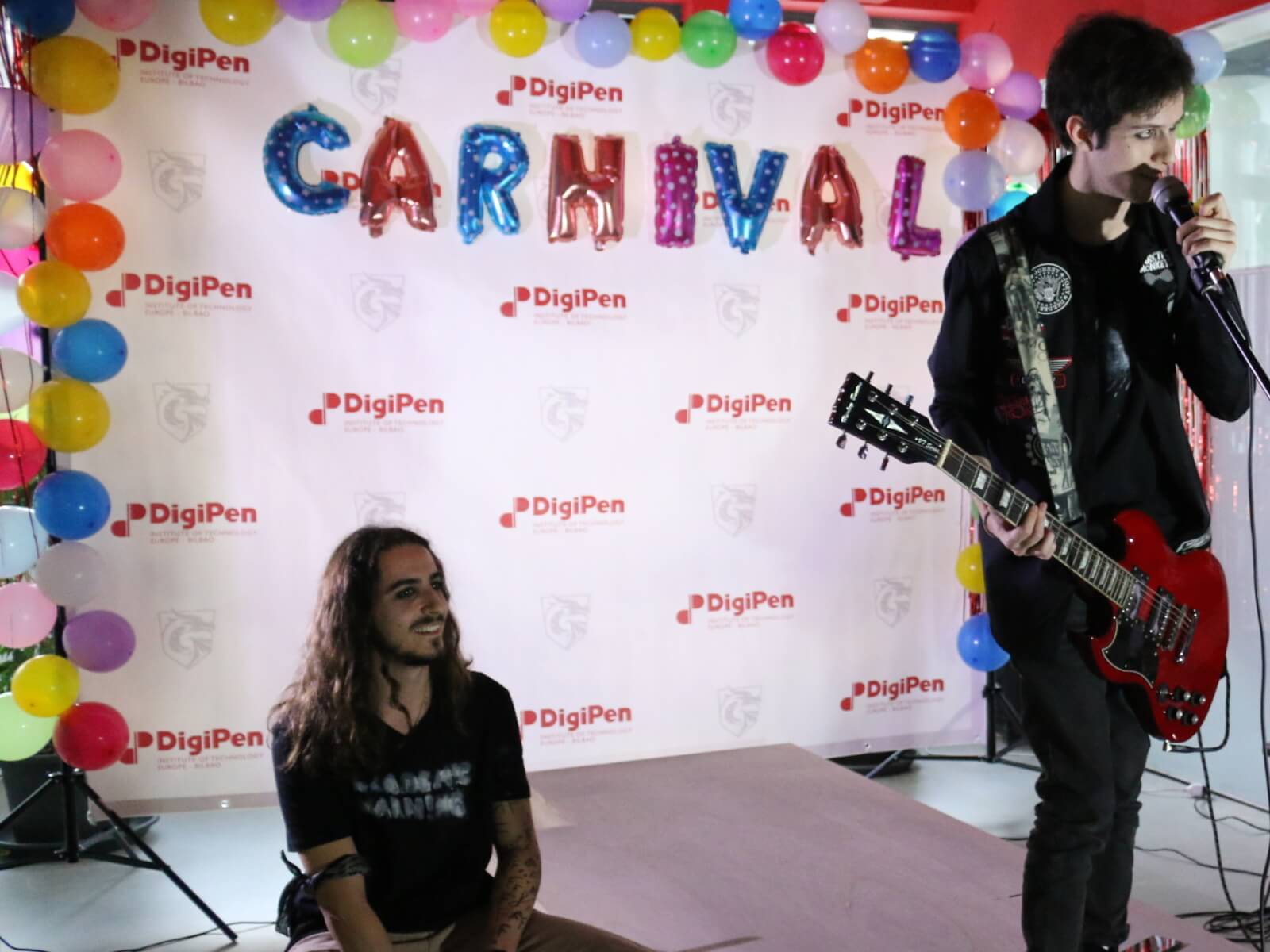 Tres miembros del grupo de música estudiantil actúan en un escenario con la palabra 'Carnaval' detrás de ellos