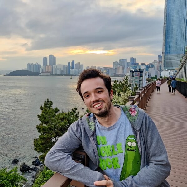 DigiPen alumnus Jon Zapata leans against a railing set against a city skyline next to water
