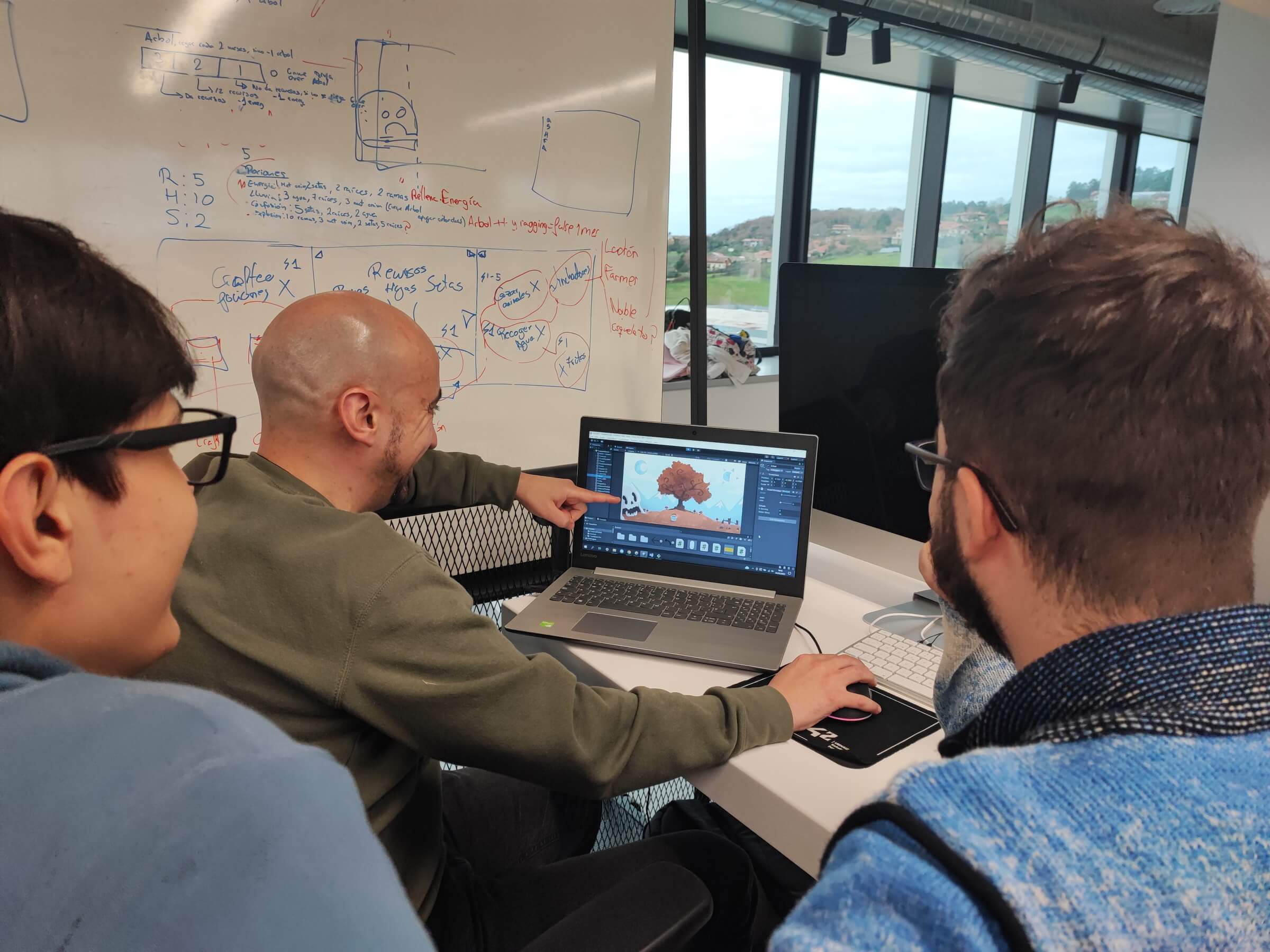 Tres desarrolladores sentados alrededor de un ordenador portátil y mientras miran un juego que se está desarrollando en el motor de juegos de Unity